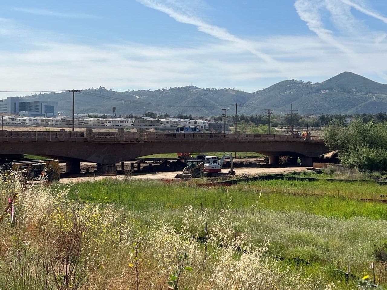 Bridge span viewed from the creek bed with excavators working below.