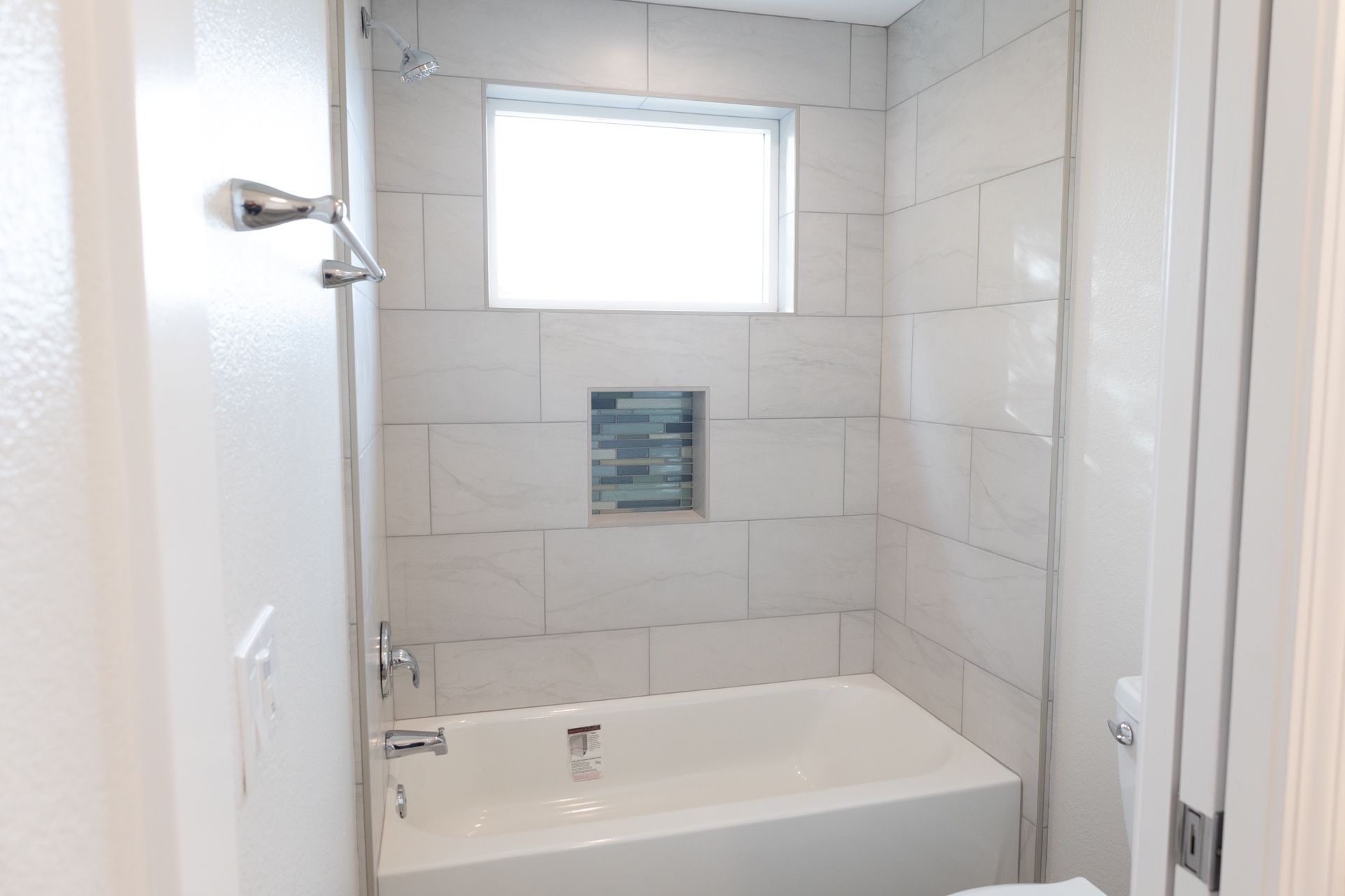 Tub-shower combo with large-format tile, glass mosaic niche, and chrome fixtures.