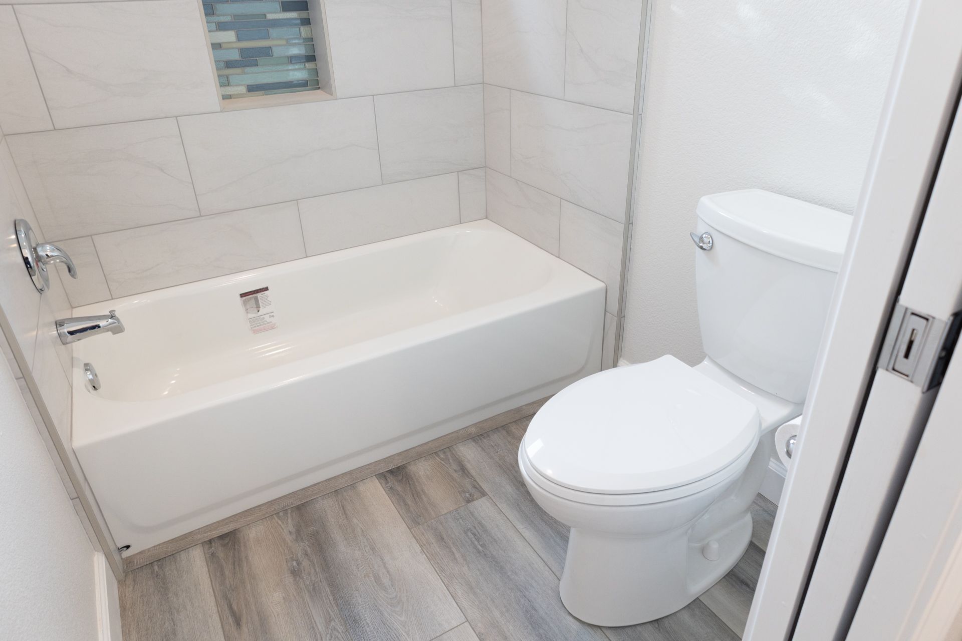 New bathroom with tiled tub, toilet, and gray wood-look plank flooring.