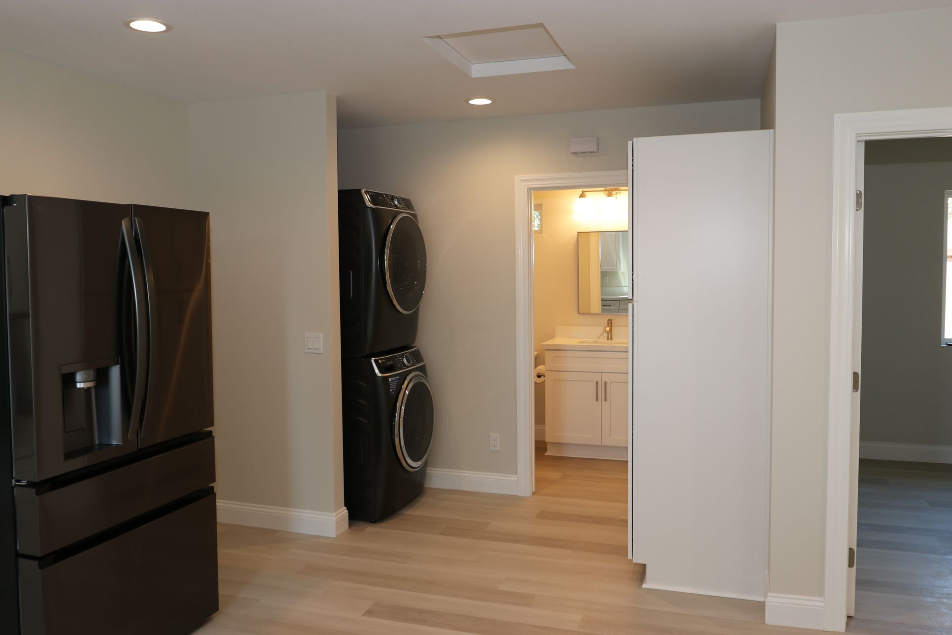 Stacked washer-dryer nook beside bathroom entry with black stainless fridge.