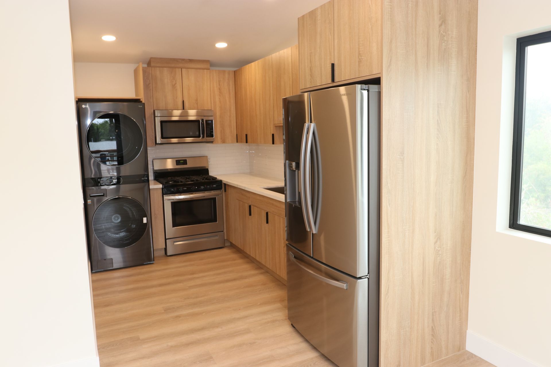 Light oak kitchen with stainless appliances and stacked washer-dryer nook.