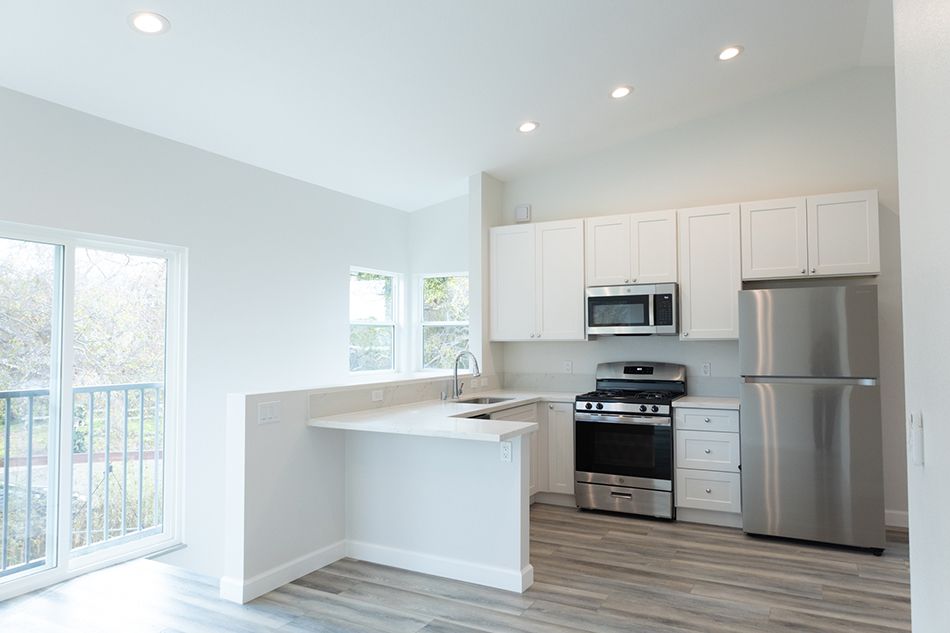 ADU kitchen with white shaker cabinets, stainless fridge and gas range, quartz peninsula, and vaulted ceiling.