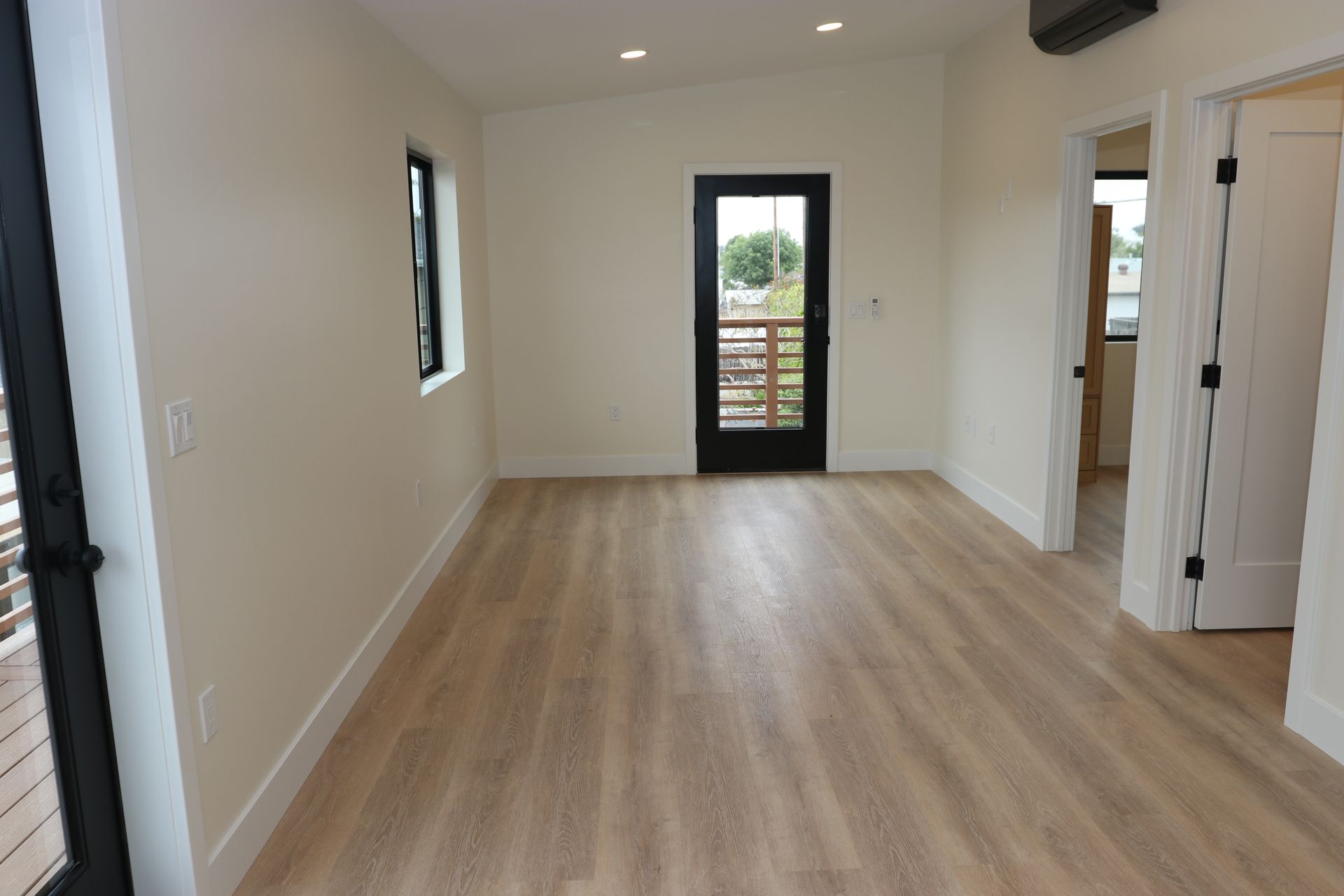 Empty living area with wood-look flooring and black glass door to balcony.