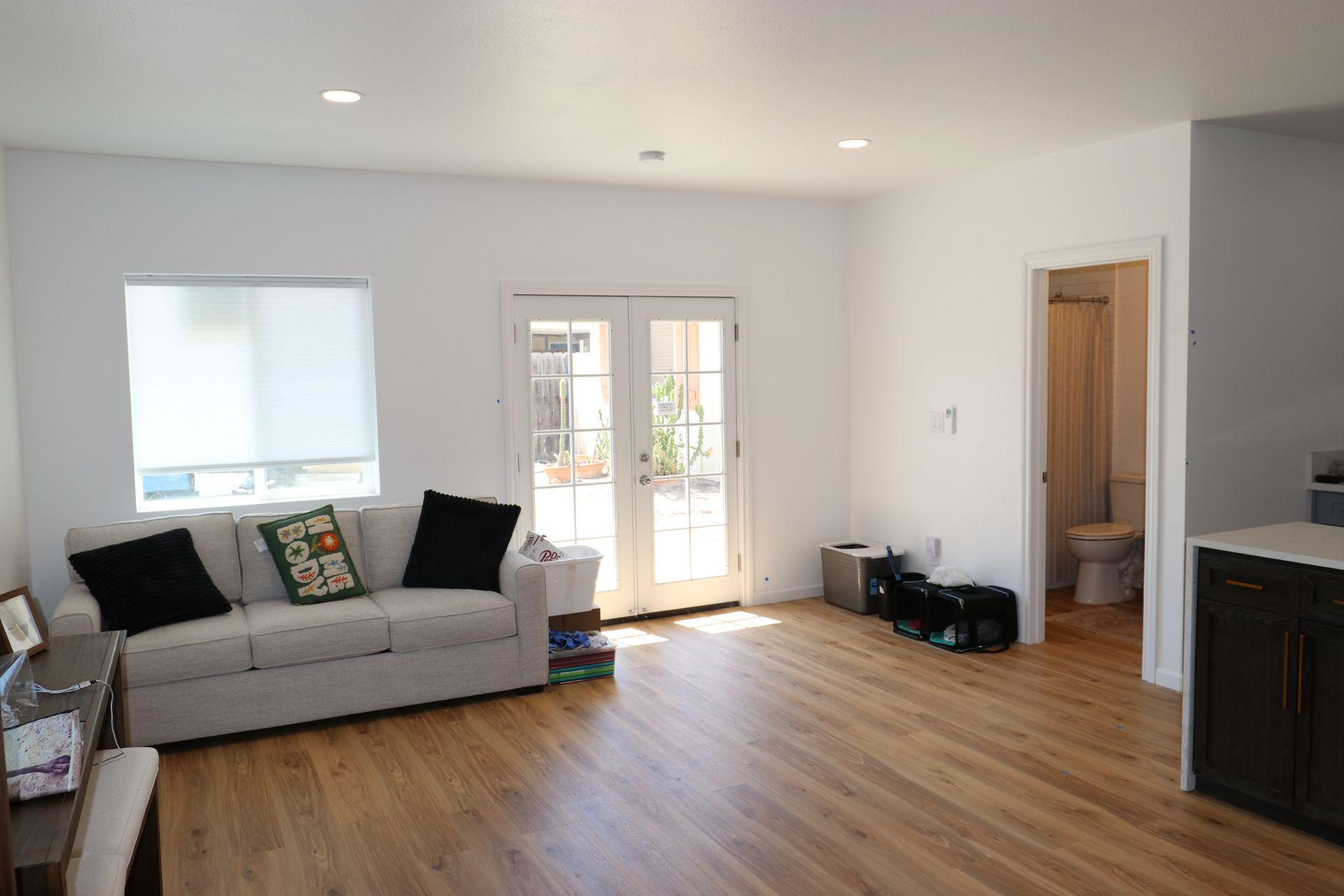 Furnished living room with beige sofa, french doors to a patio, and warm wood-look plank flooring.