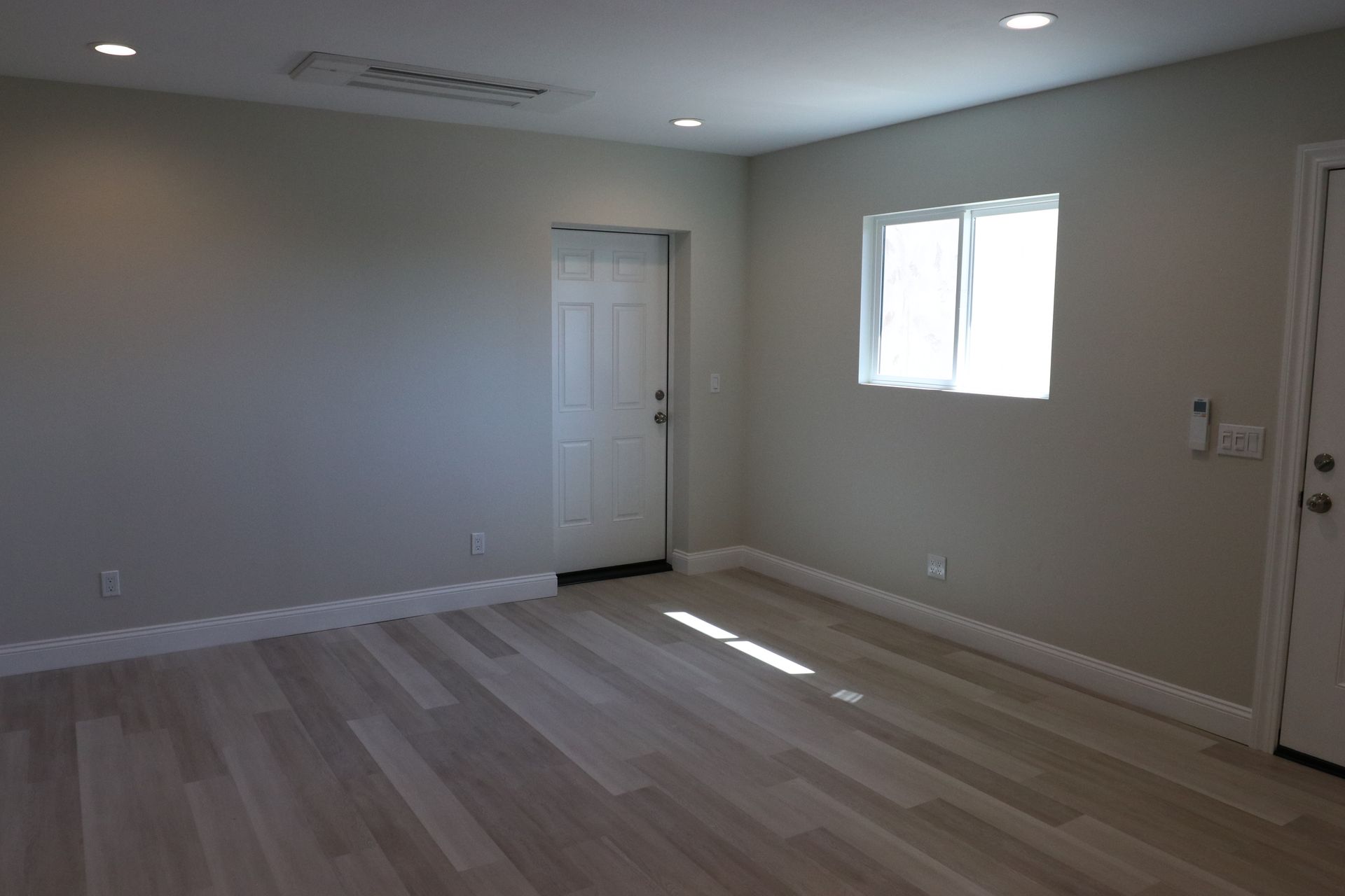 Empty living room with gray walls, white entry door, and wood-look flooring.