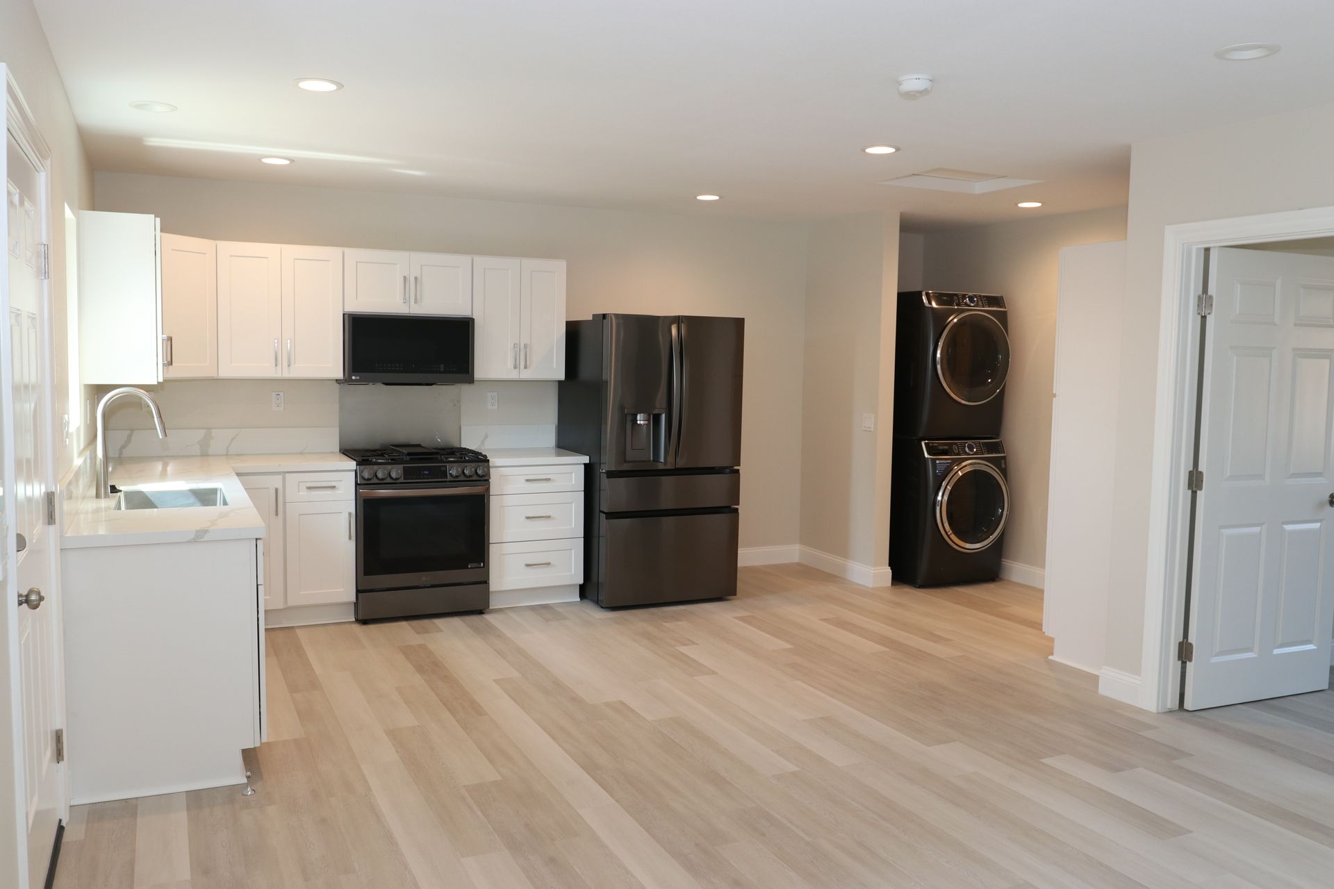Open-concept white kitchen with black stainless fridge and stacked washer-dryer.