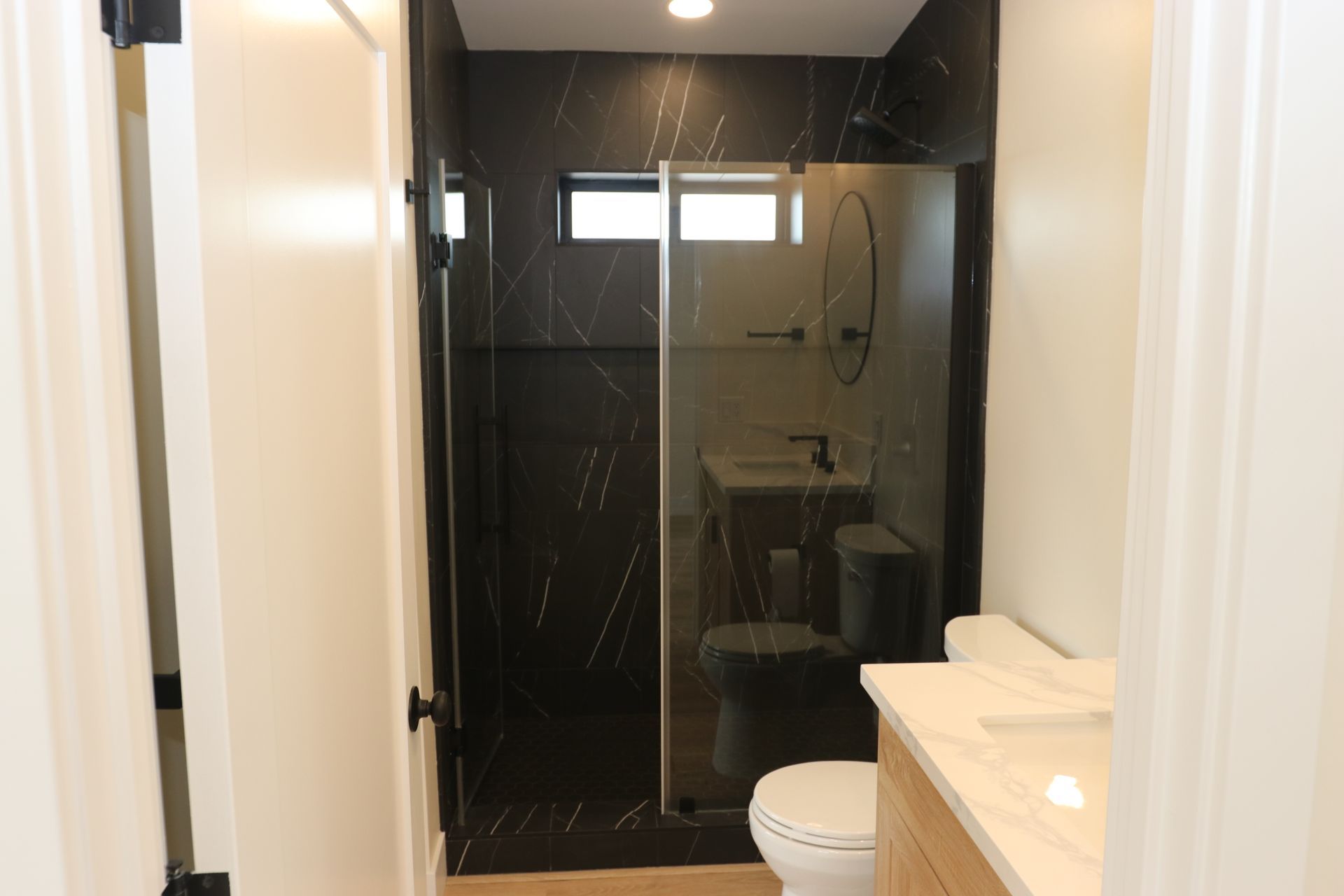 Bathroom with black marble-look tile walk-in shower and glass door.