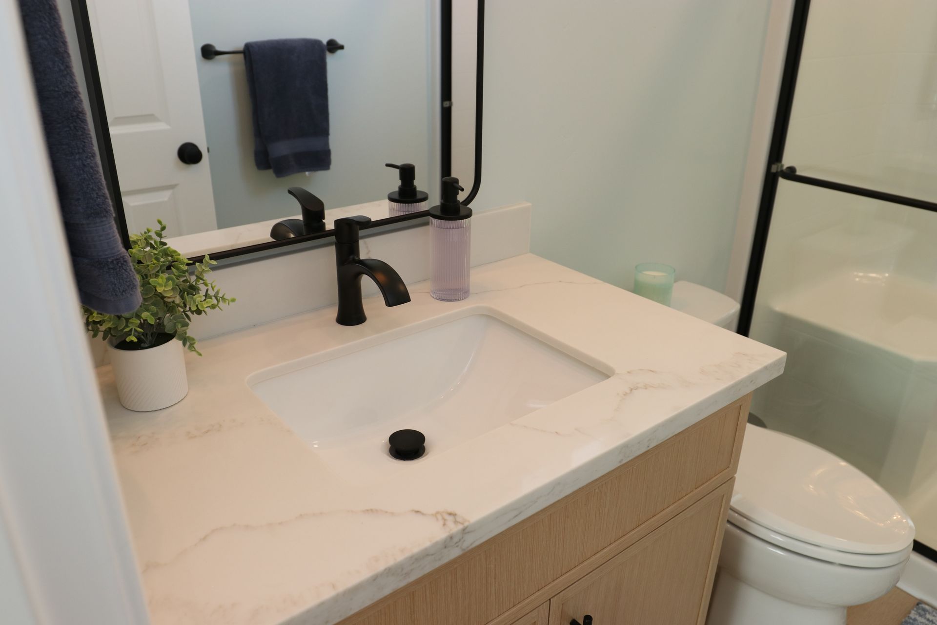 Bathroom with white oak vanity, quartz top, matte black faucet, and glass-enclosed shower.