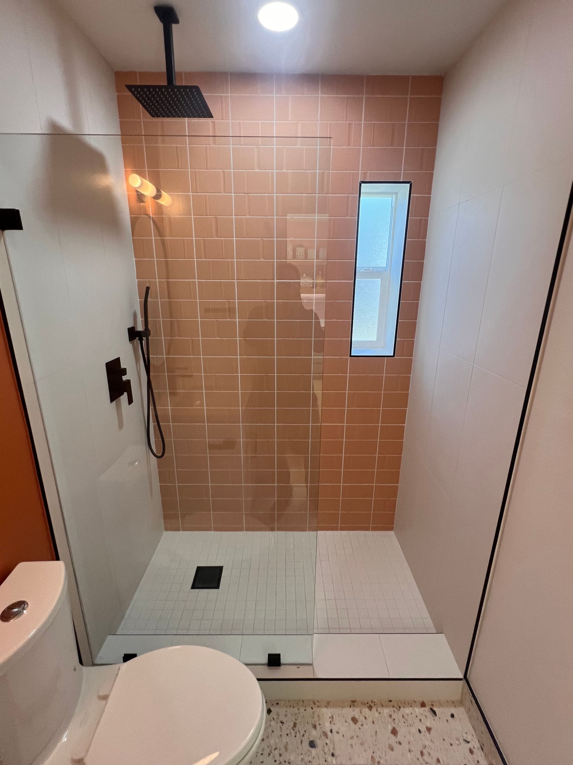 Walk-in shower with pink square tile, black rain shower head, and terrazzo floor accents.