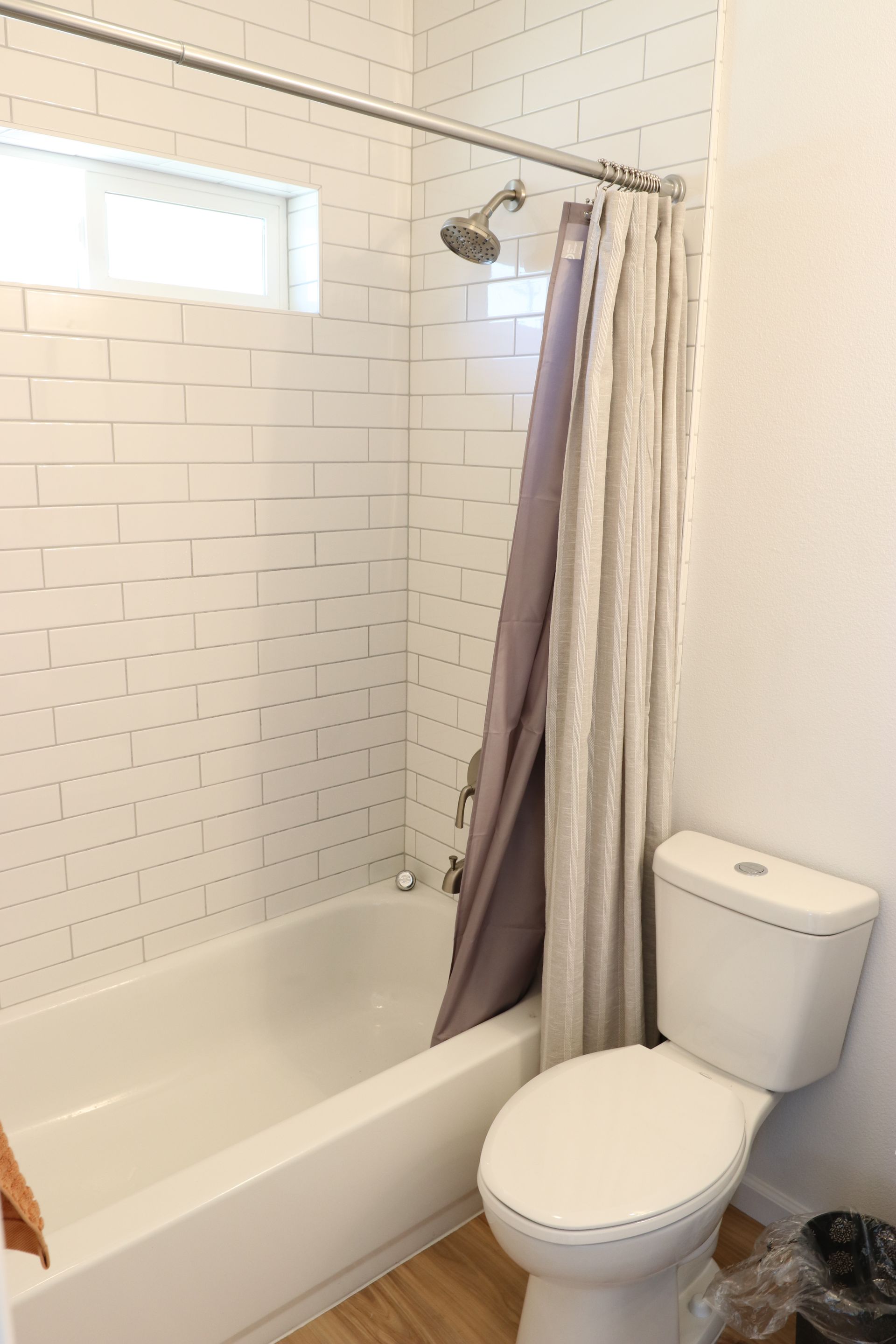 Tub-shower combo with white subway tile surround, brushed nickel fixtures, and a small privacy window.