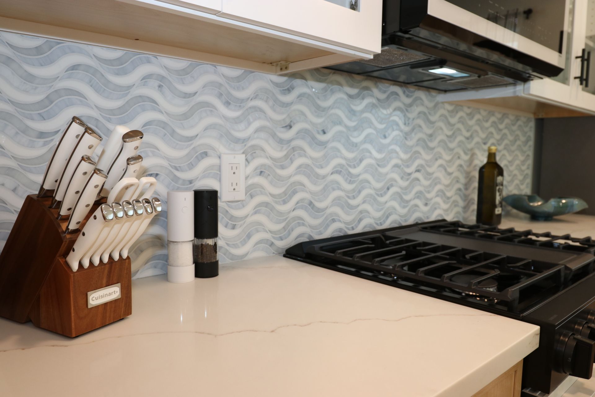 Detail of blue wave mosaic backsplash above quartz counter next to the gas range.