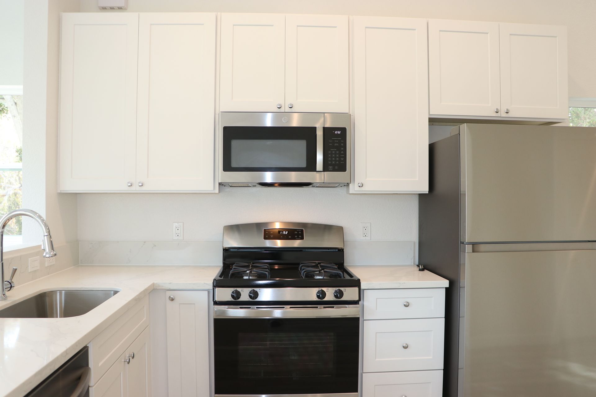 Kitchen with stainless gas range and over-range microwave flanked by white shaker cabinets and a stainless fridge.
