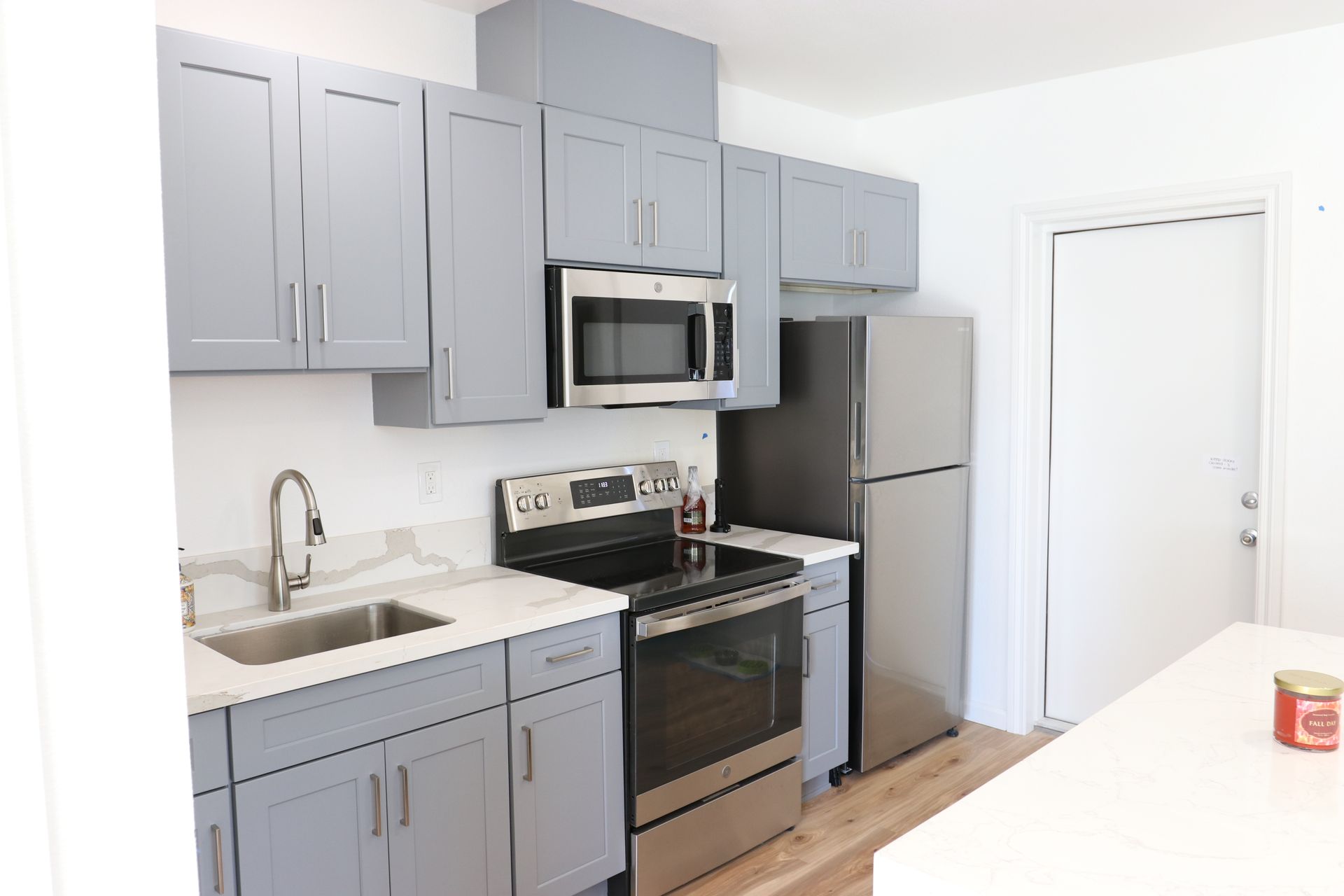 Kitchen with gray shaker cabinets, stainless electric range, microwave, fridge, and quartz counters.