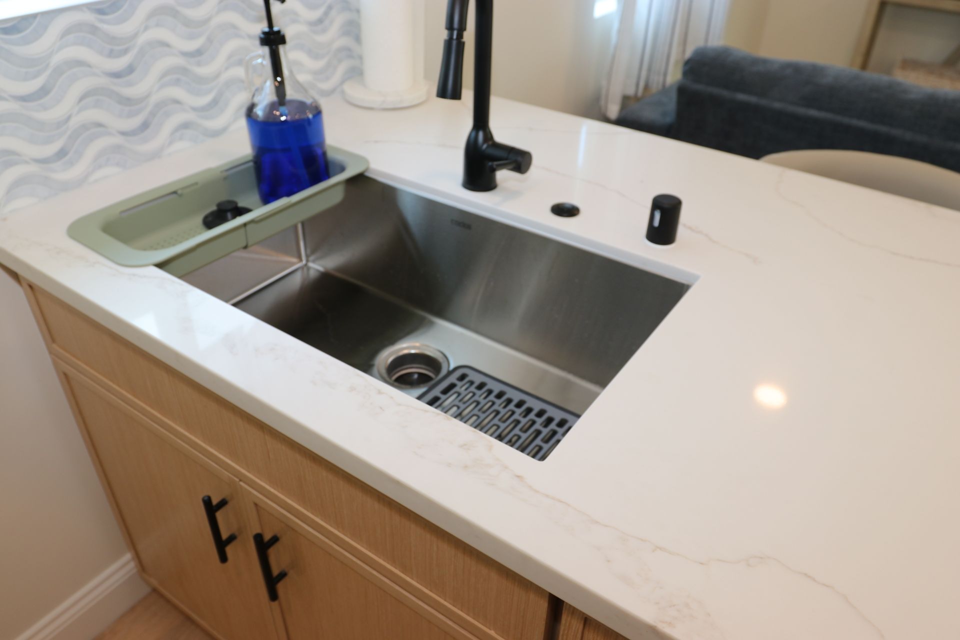 Close-up of stainless undermount island sink with matte black faucet and white quartz counter.