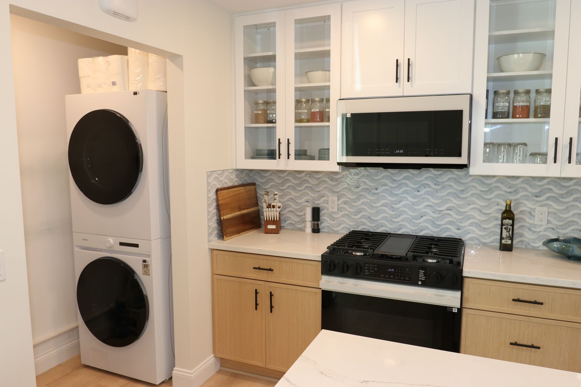 Kitchen with blue wave-tile backsplash, black gas range, and stacked washer-dryer nook.