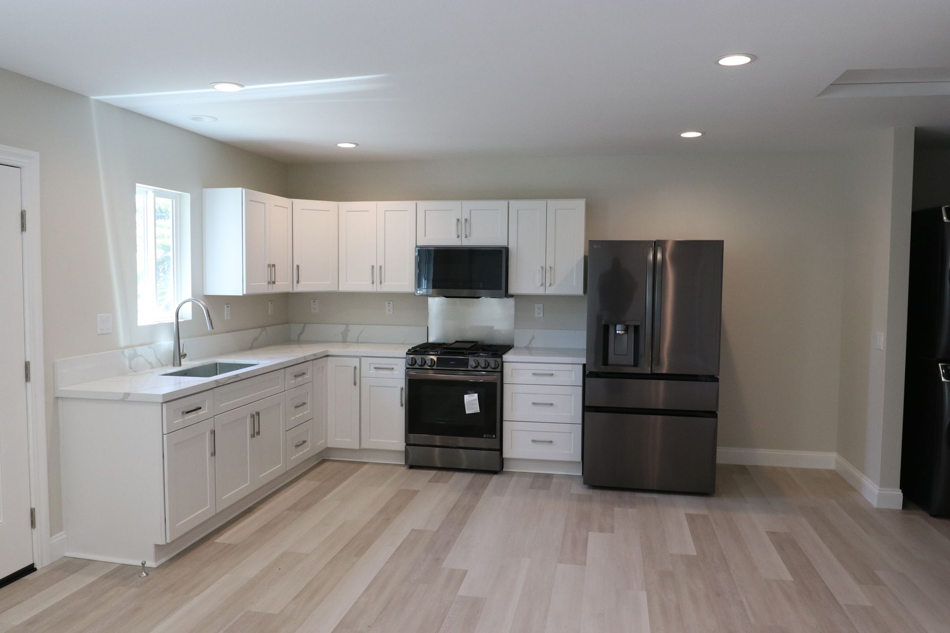 White shaker kitchen with quartz counters and black stainless appliances.