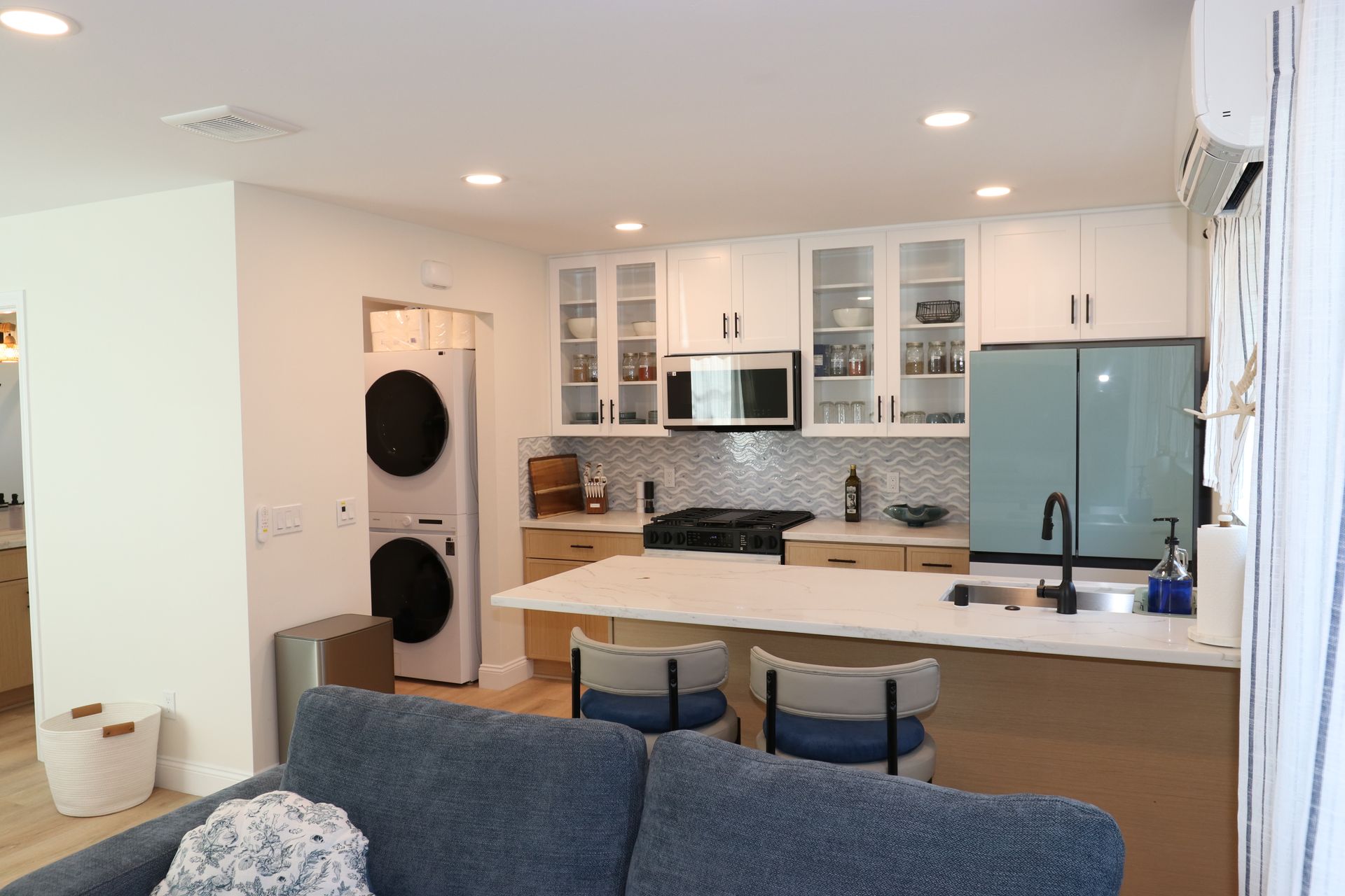 Open-concept studio kitchen with quartz island, teal refrigerator, and stacked washer-dryer closet.