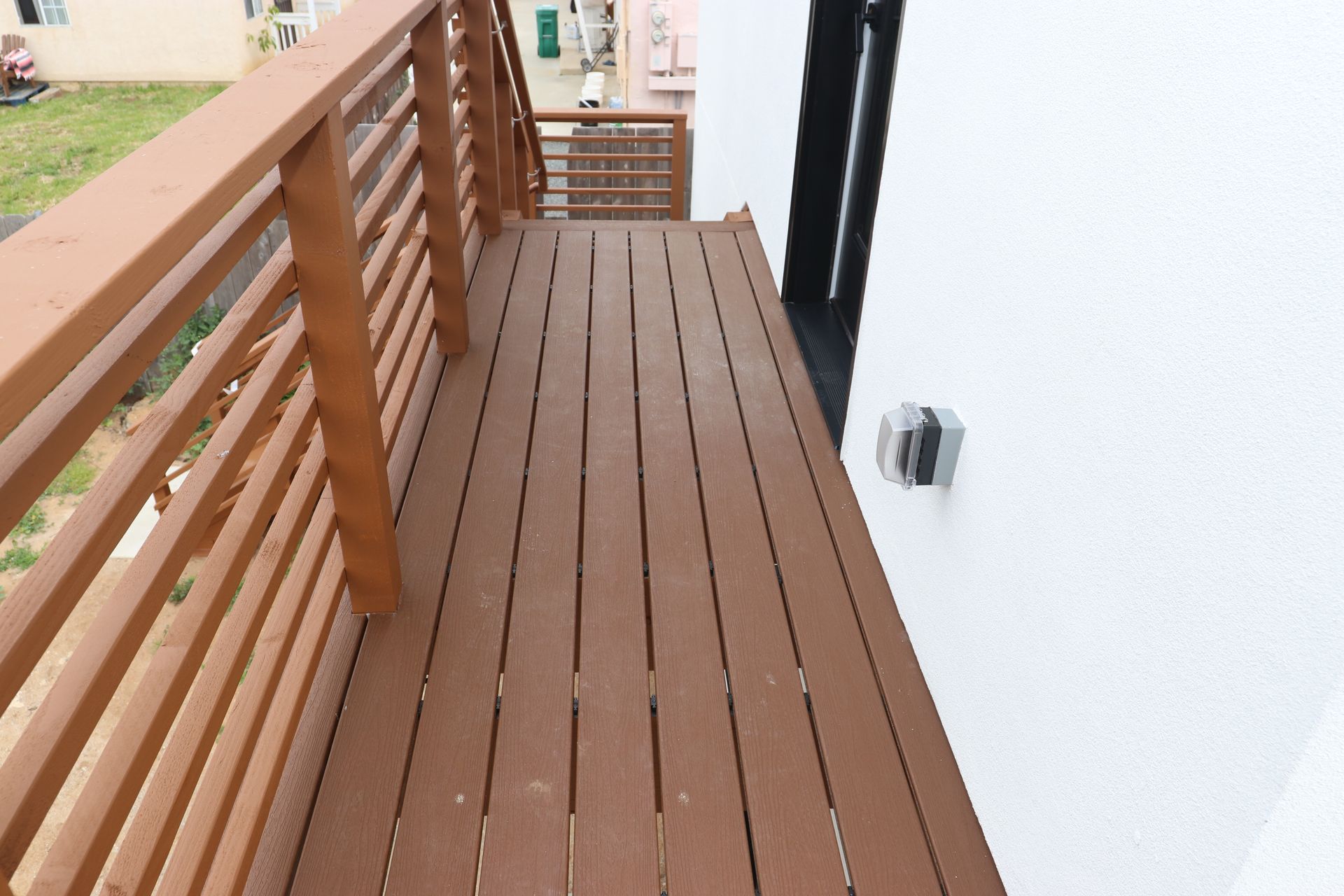 Second-story wood balcony deck with brown-stained horizontal railing.