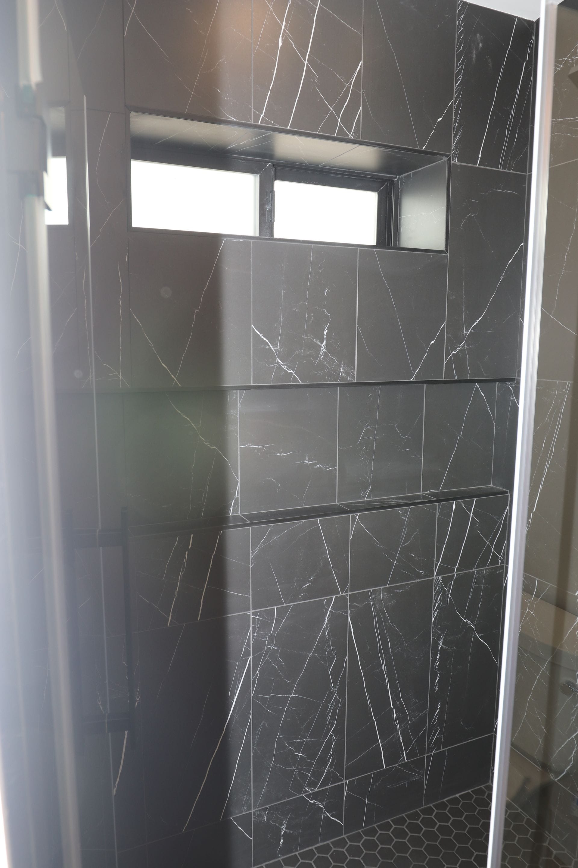 Black marble-look tile shower with recessed niches and transom window.