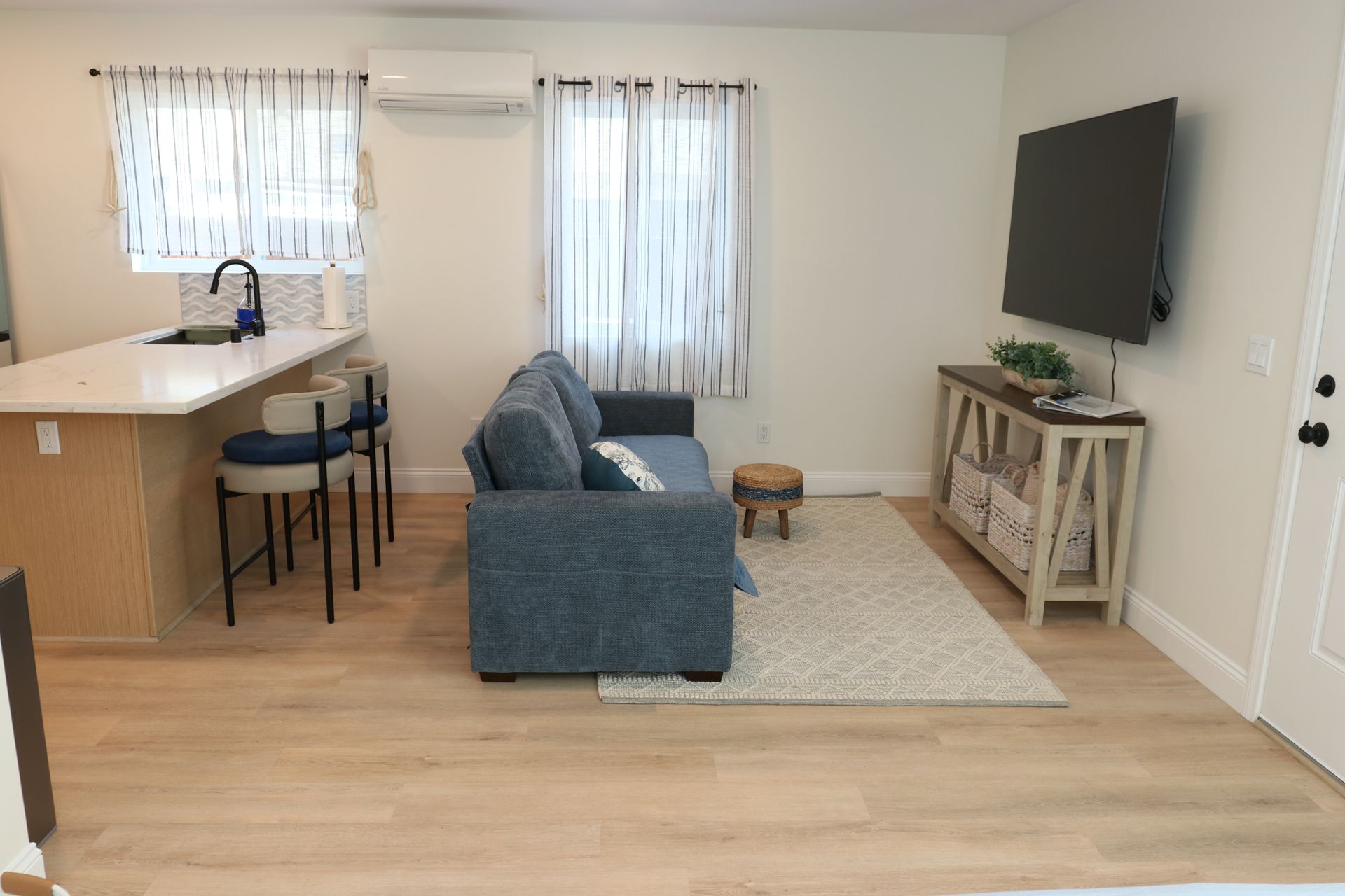 Studio living area with blue sofa, wall-mounted TV, mini-split, and breakfast bar seating.
