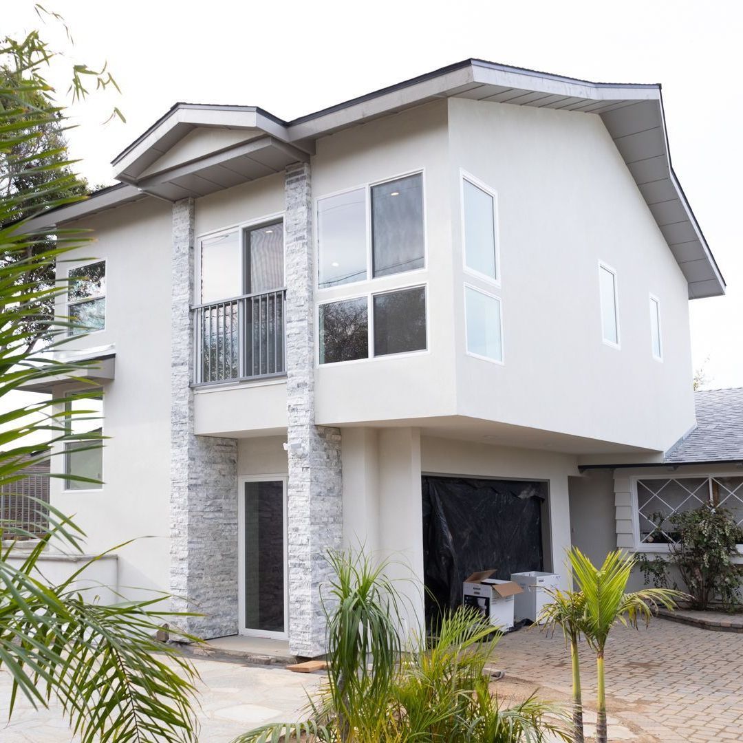 Two-story white ADU above a garage with stacked stone columns and balcony.