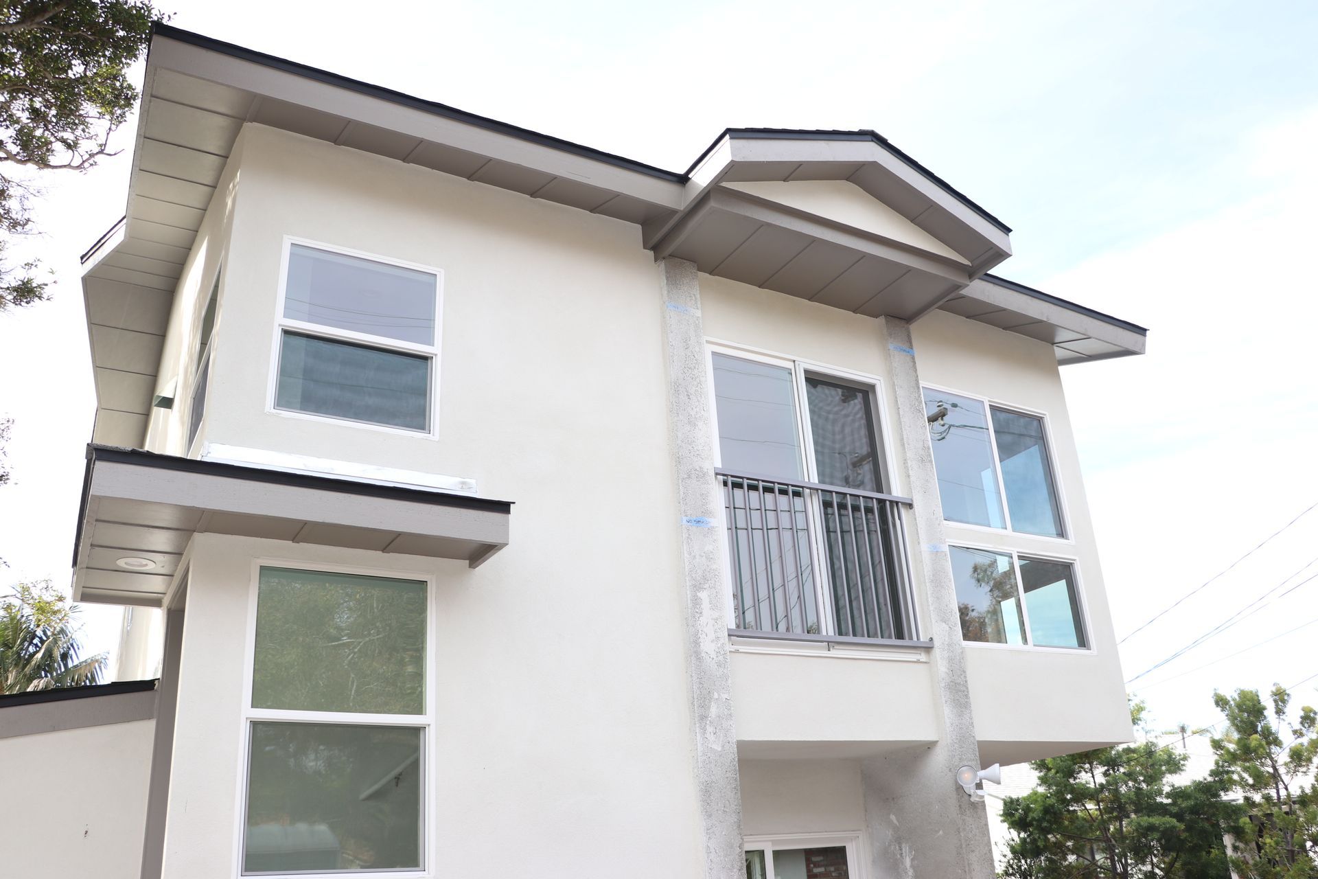 Upward view of a two-story white stucco ADU with juliet balcony and gray fascia nearing completion.
