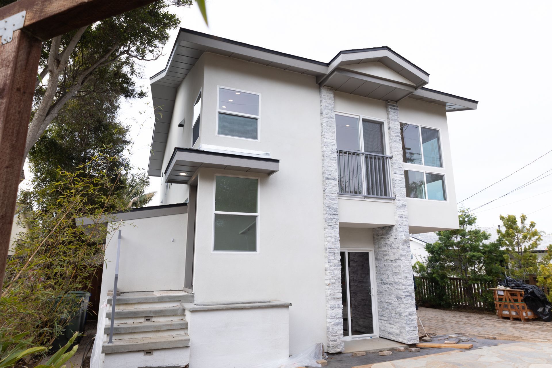 Completed two-story white stucco ADU with stacked-stone accent columns, balcony, and exterior stairs.