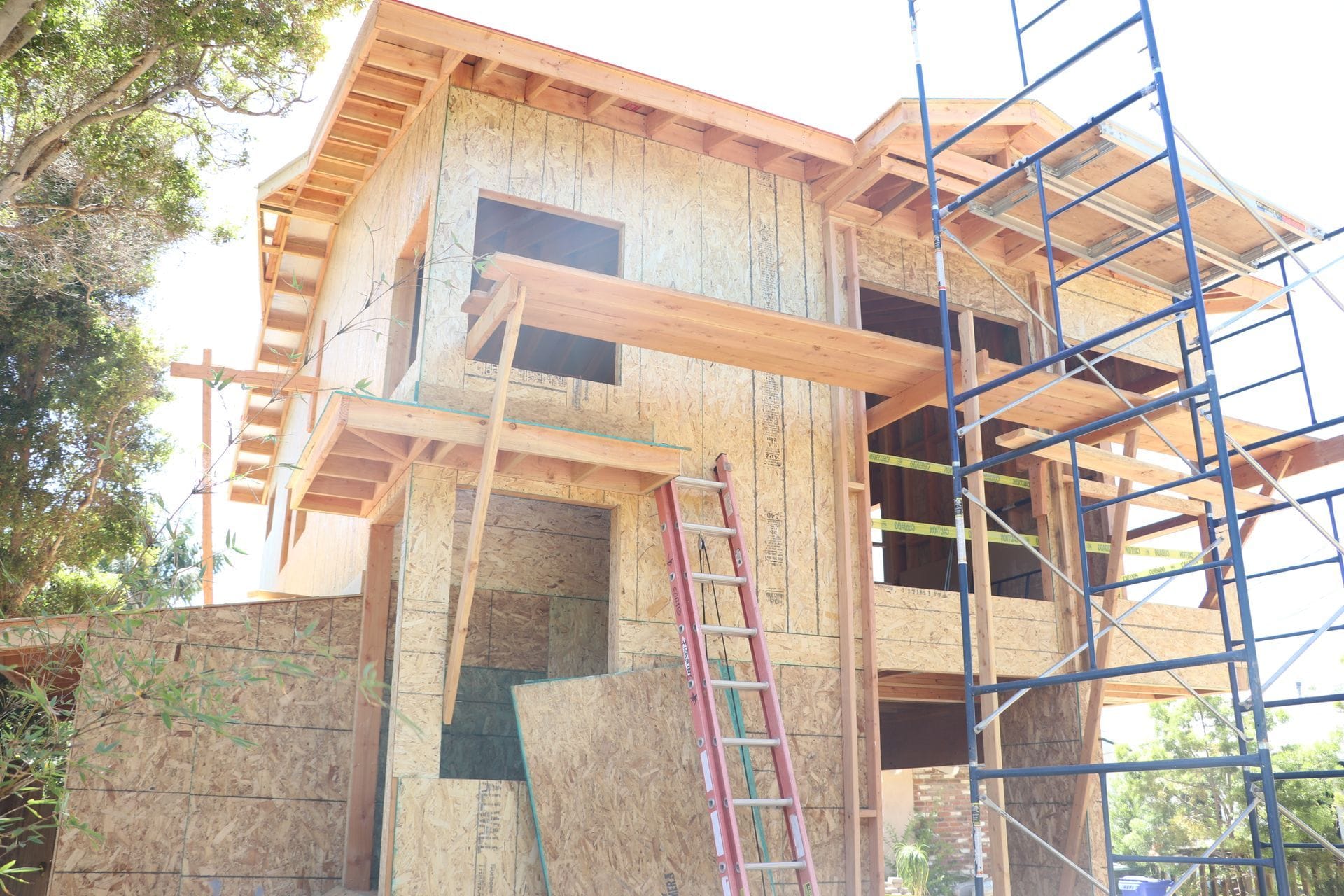 Two-story ADU under construction with wood framing, plywood sheathing, ladder, and scaffolding.